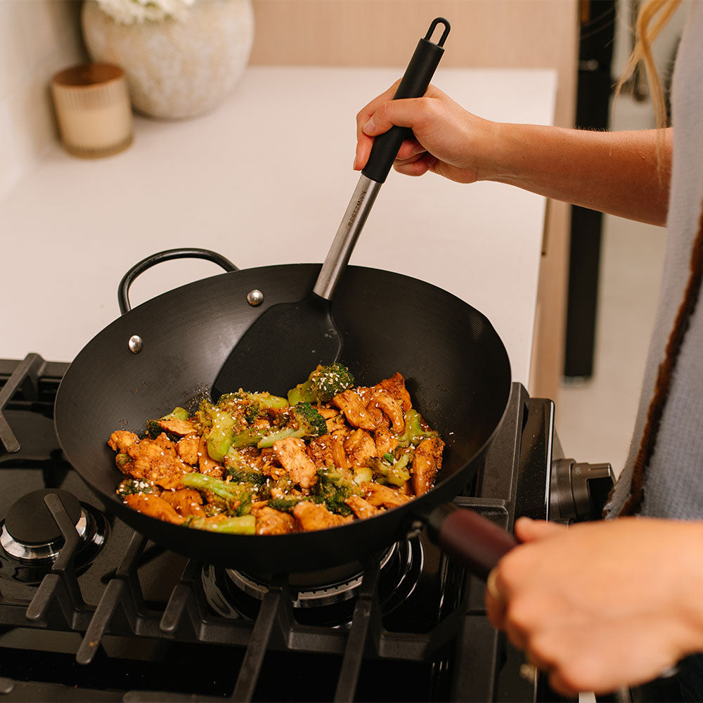 Person stirring Sesame Chicken with broccoli in a wok pan.