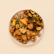Overhead shot of a plated meal featuring glazed meatballs, sliced pineapple, zucchini, and brown rice on a light beige plate against a solid cream background.