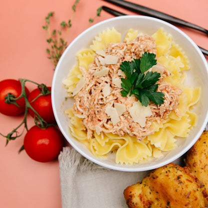 Bow tie pasta with Beehive Meals Tuscan Chicken in a white bowl on a pink background.