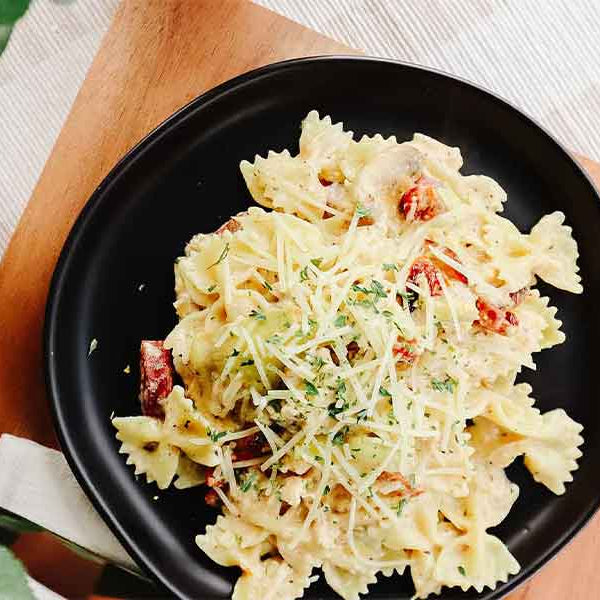 Black plate with Beehive Meals Zesty Italian Chicken with bowtie pasta on a wooden surface