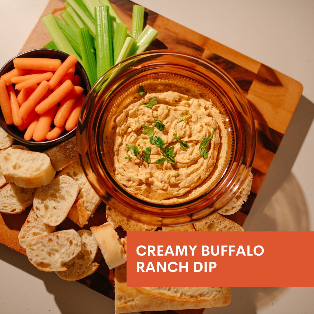 Creamy buffalo ranch dip with carrots, celery, and bread on a wooden board.