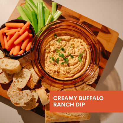 Creamy buffalo ranch dip with carrots, celery, and bread on a wooden board.