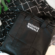 Black bag with 'Beehive & Meals' logo on a checkered blanket