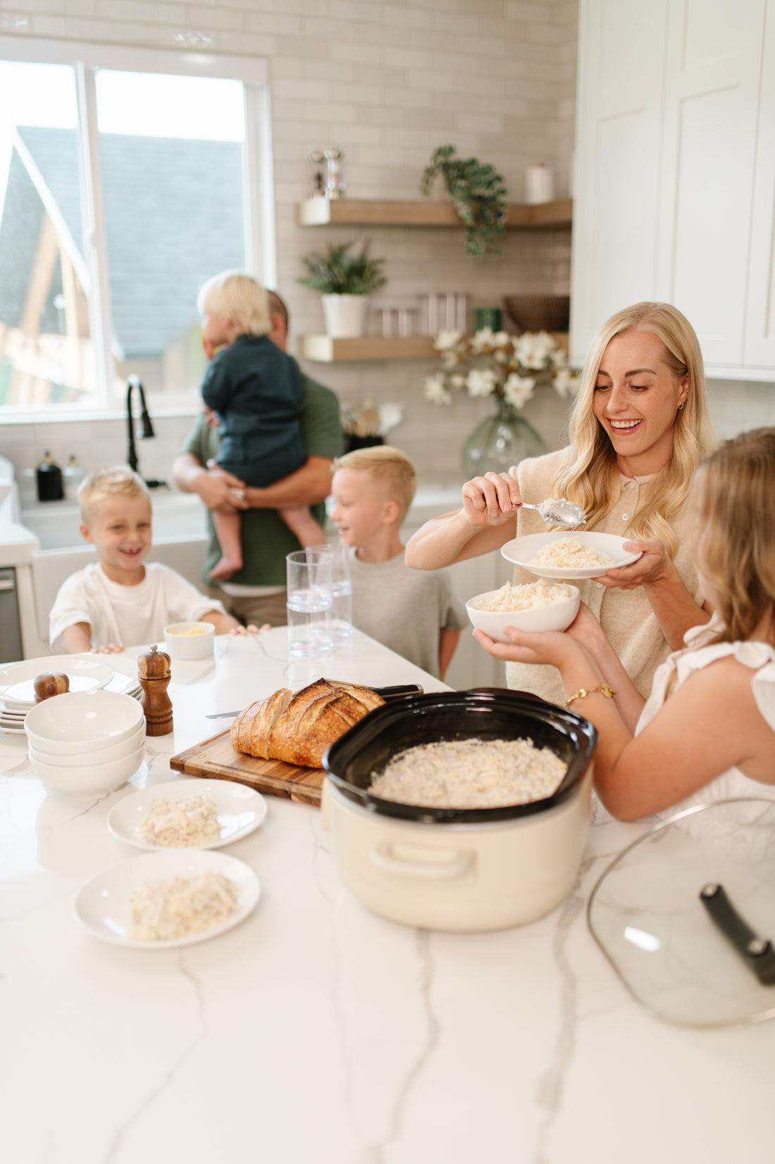 Allyse Jackson Founder, and family preparing a meal in a bright, modern kitchen. In the foreground, a cream-colored slow cooker filled with rice sits on a white marble table, alongside plates, bowls, and a loaf of bread.