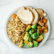 Plate of Beehive Meals Apple Cider Pork Roast with brussels sprouts, carrots and rice on a white background