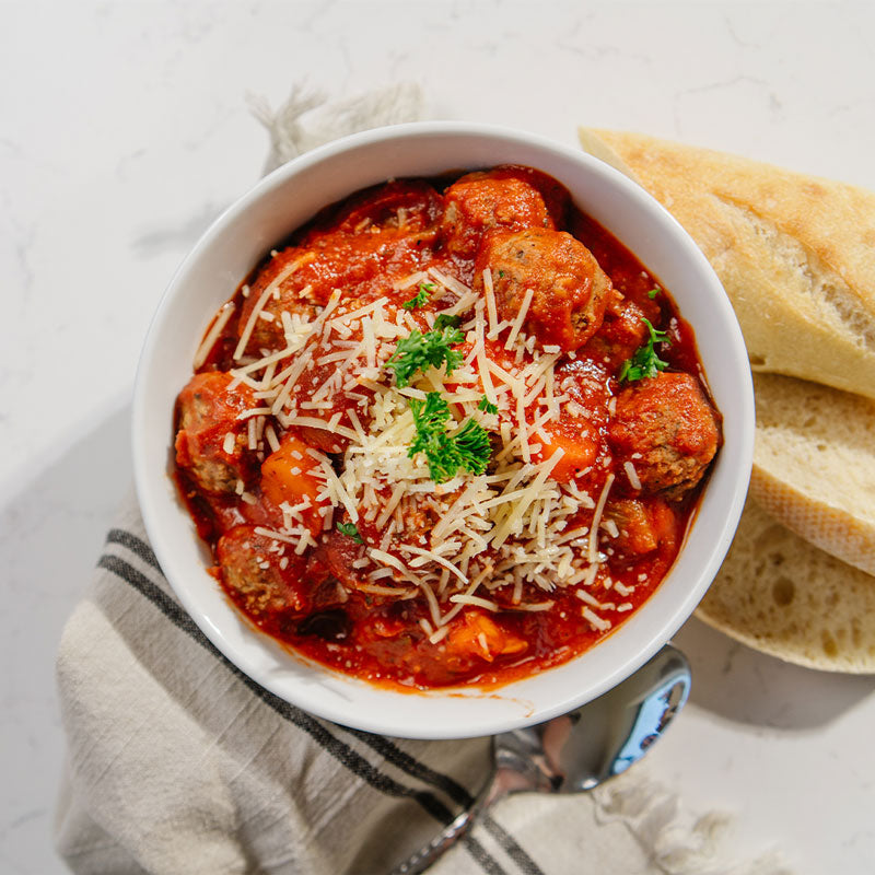 Bowl of meatball soup with bread on a light background