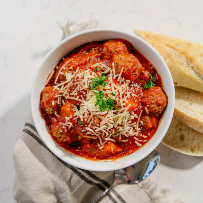 Bowl of meatball soup with bread on a light background