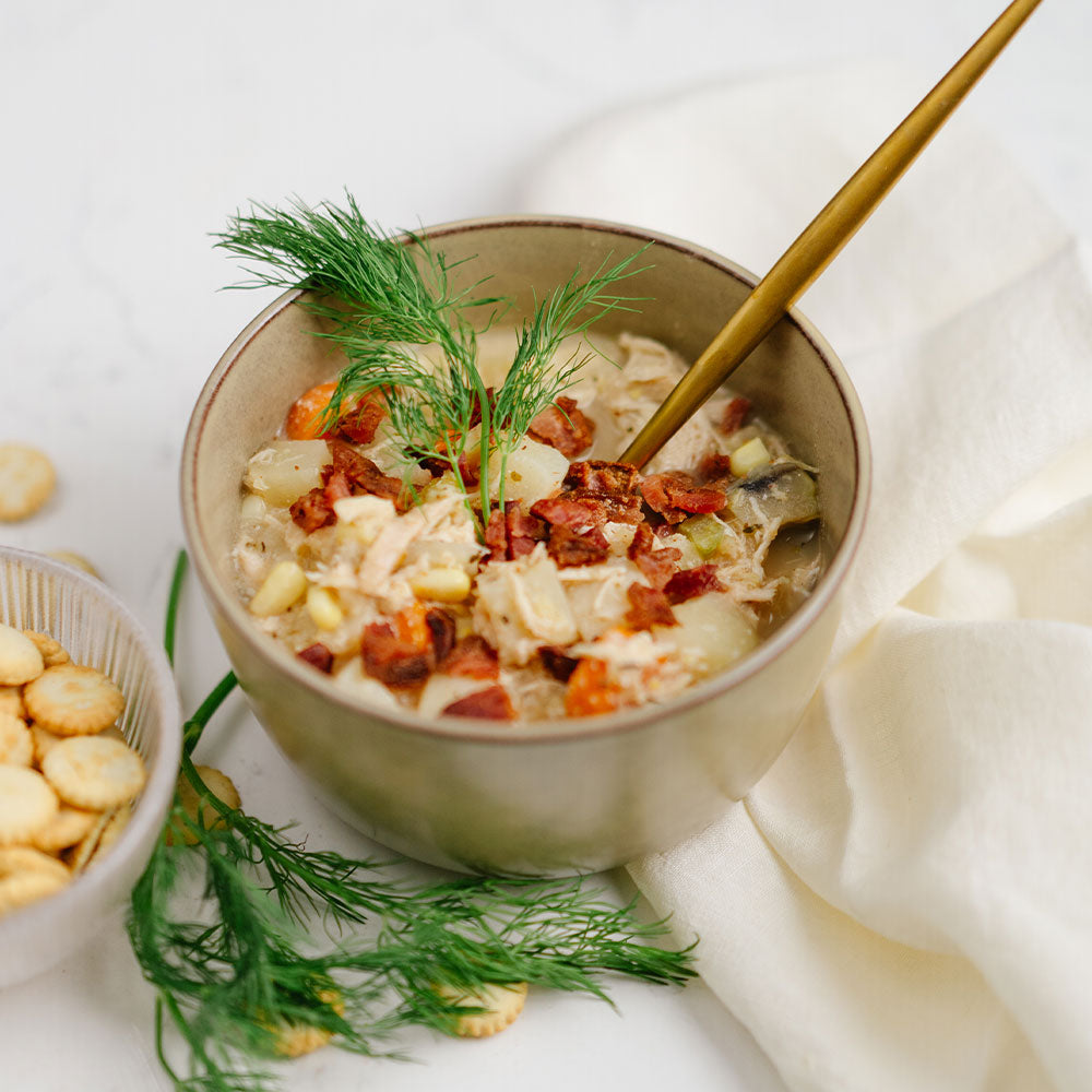Bowl of soup with crackers and dill on a white surface