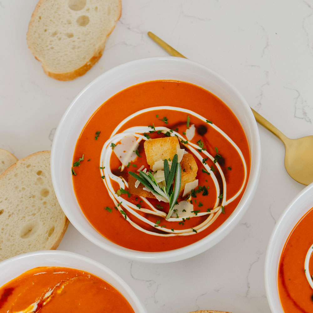 Tomato soup with croutons and herbs in a white bowl on a marble surface.