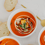 Tomato soup with croutons and herbs in a white bowl on a marble surface.